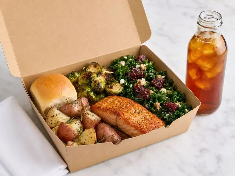 Mountain View corporate boxed dinner by Winslow’s Catering with a salmon fillet, seasonal sides, leafy greens, bread, and a chilled beverage.