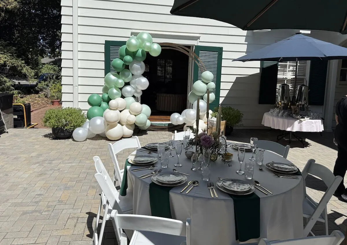 Sage and ivory balloon arch over an archway paired with a styled table — balloon and floral styling for Cupertino catering milestone parties
