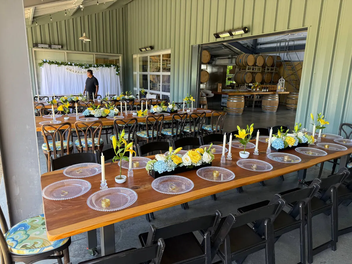 Long table lined with yellow lily, blue hydrangea and white rose centerpieces between taper candles — centerpiece design for Los Altos catering receptions